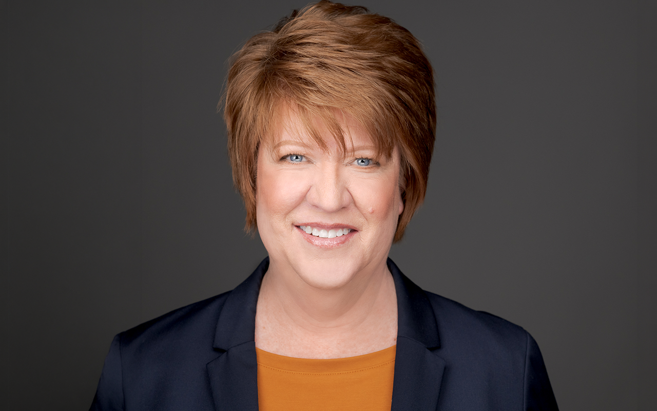 Portrait of Kris Austin, principal of KS Austin Communications, smiling in a navy blazer against a dark gray background.